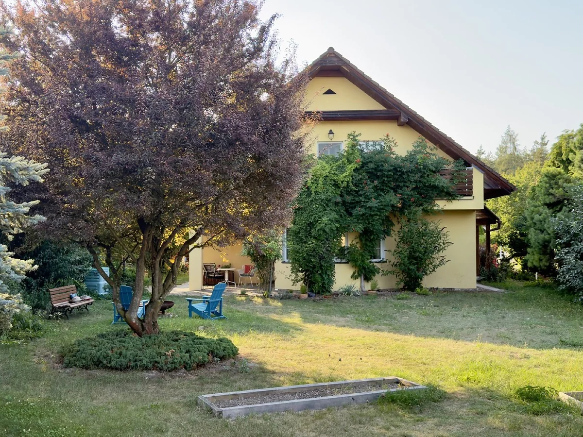 Zahrada s posezením na dřevěných křeslech pod stromem, v pozadí dům porostlý popínavou rostlinou